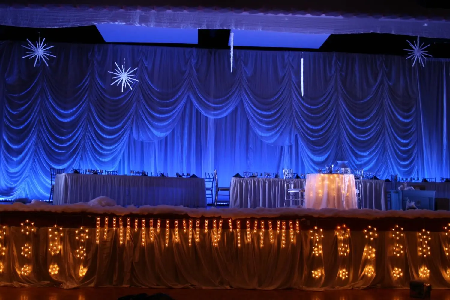 A stage decorated with blue lighting, drapes, and string lights.