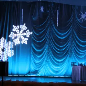 Stage decorated with large snowflakes and blue curtains, ready for a winter event.