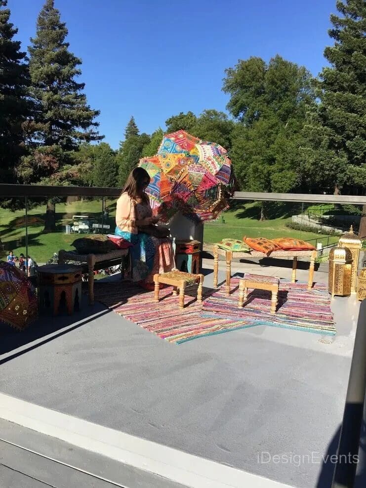 People browsing colorful rugs and crafts at an outdoor market on a sunny day.