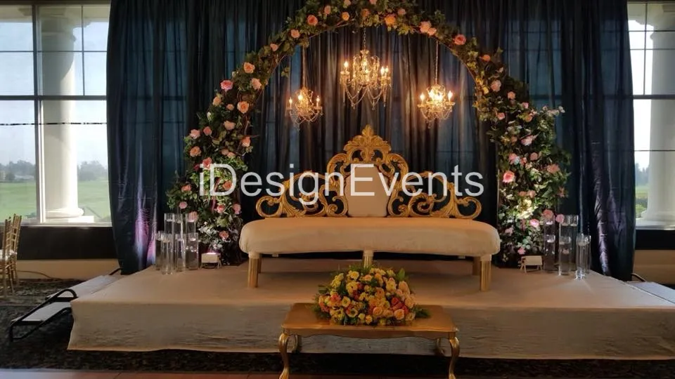 Elegant floral arch and chandelier above a white sofa on a decorated stage.