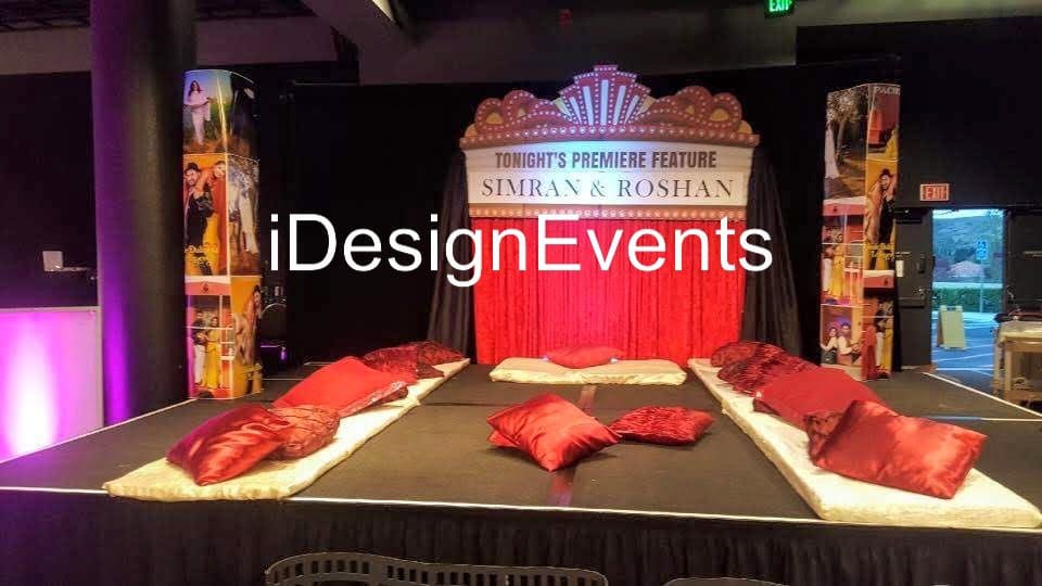 A decorated wedding stage with red cushions and a backdrop featuring a couple's photo.