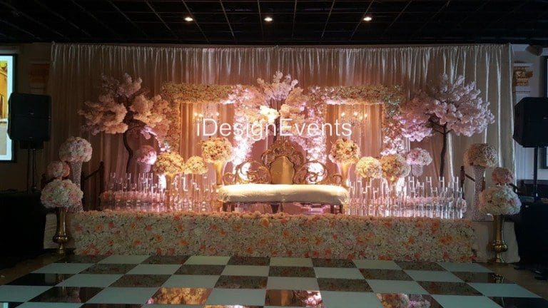 Elegant golden-themed wedding stage with floral arrangements and draped curtains.