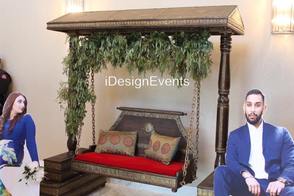 Elegant wooden swing adorned with greenery and red cushions.