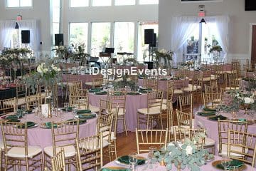 Elegant event setup with gold chairs and floral centerpieces in a bright room.