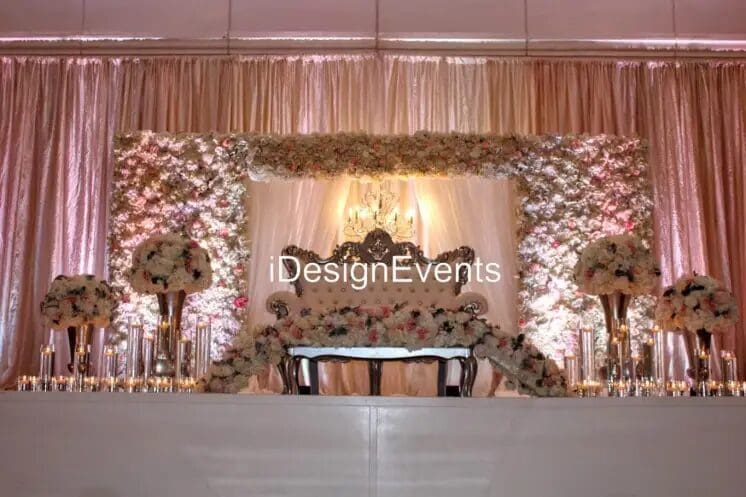 Elegant wedding stage with floral backdrop and white drapes.