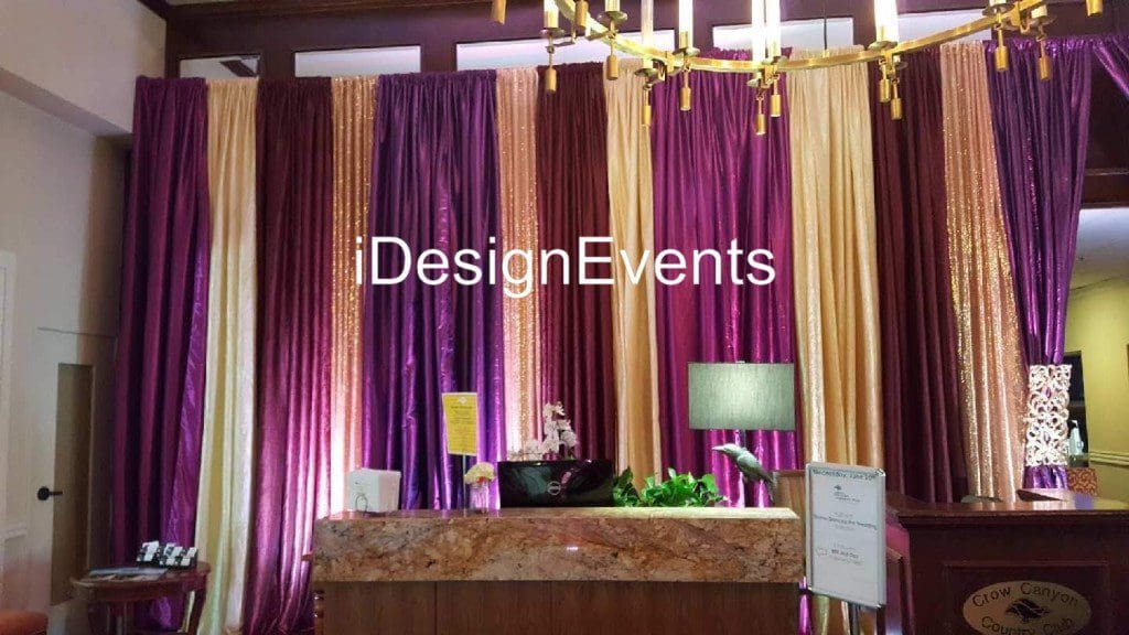 Elegant event backdrop with purple and gold drapes and ambient lighting.