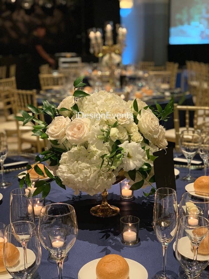 Elegant floral centerpiece with white flowers and greenery on a dark tablecloth.