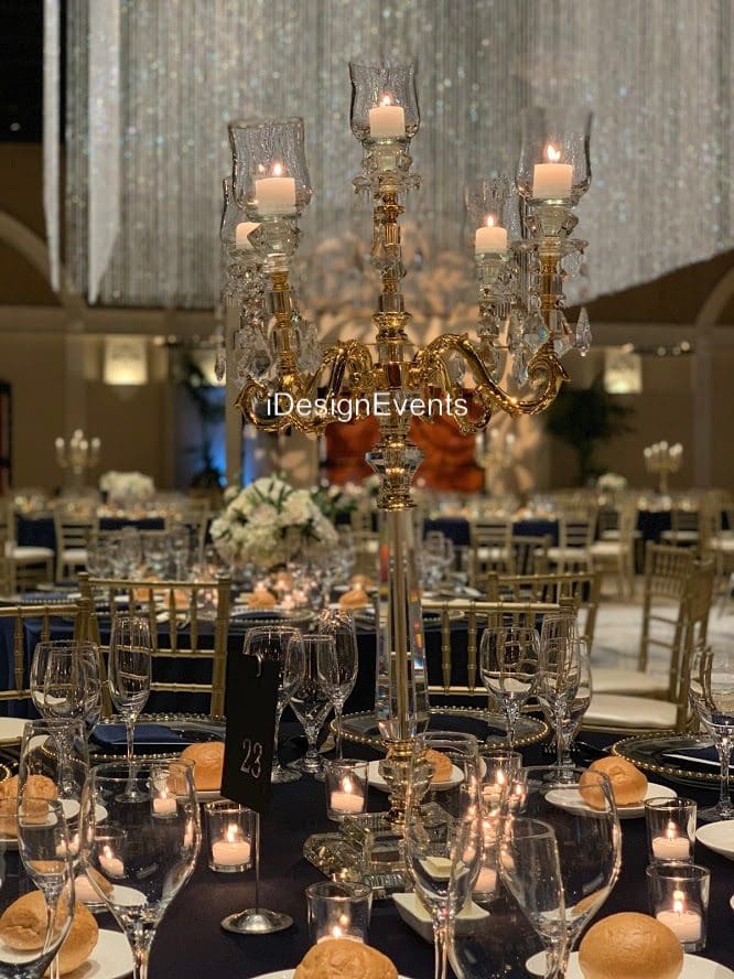 Elegant event table setup with gold chairs and floral centerpieces under candlelight.
