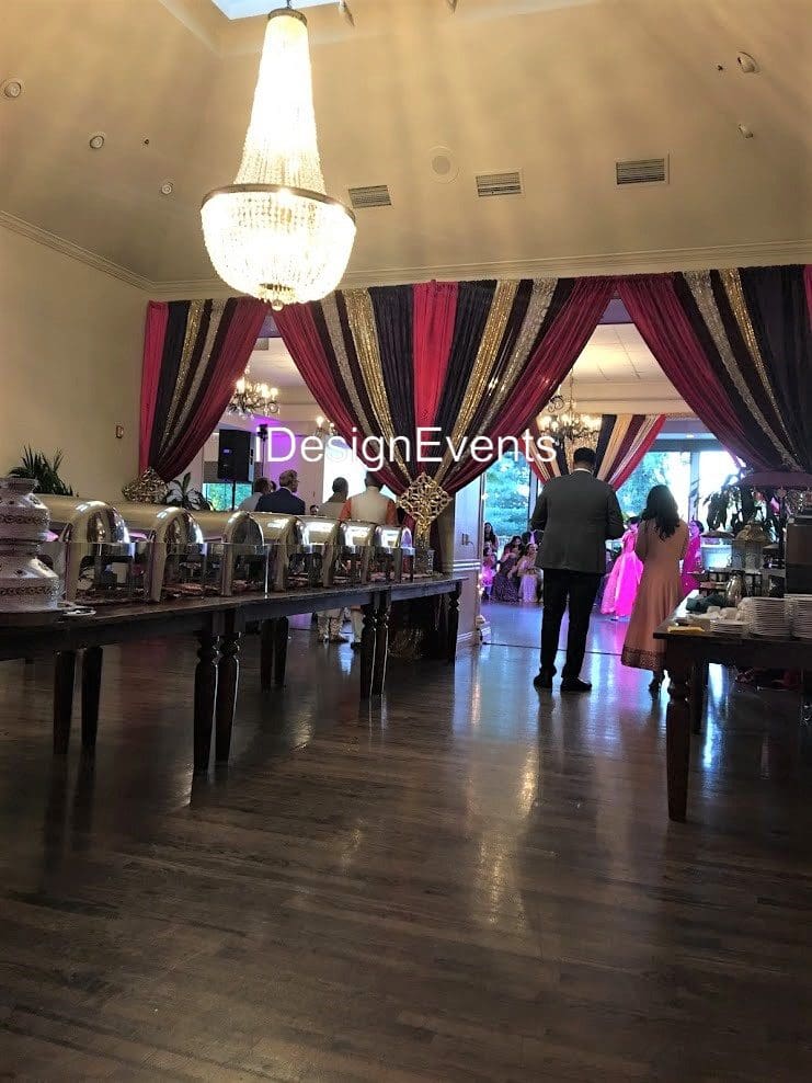 Elegant indoor wedding reception setup with wooden floors and burgundy curtains.