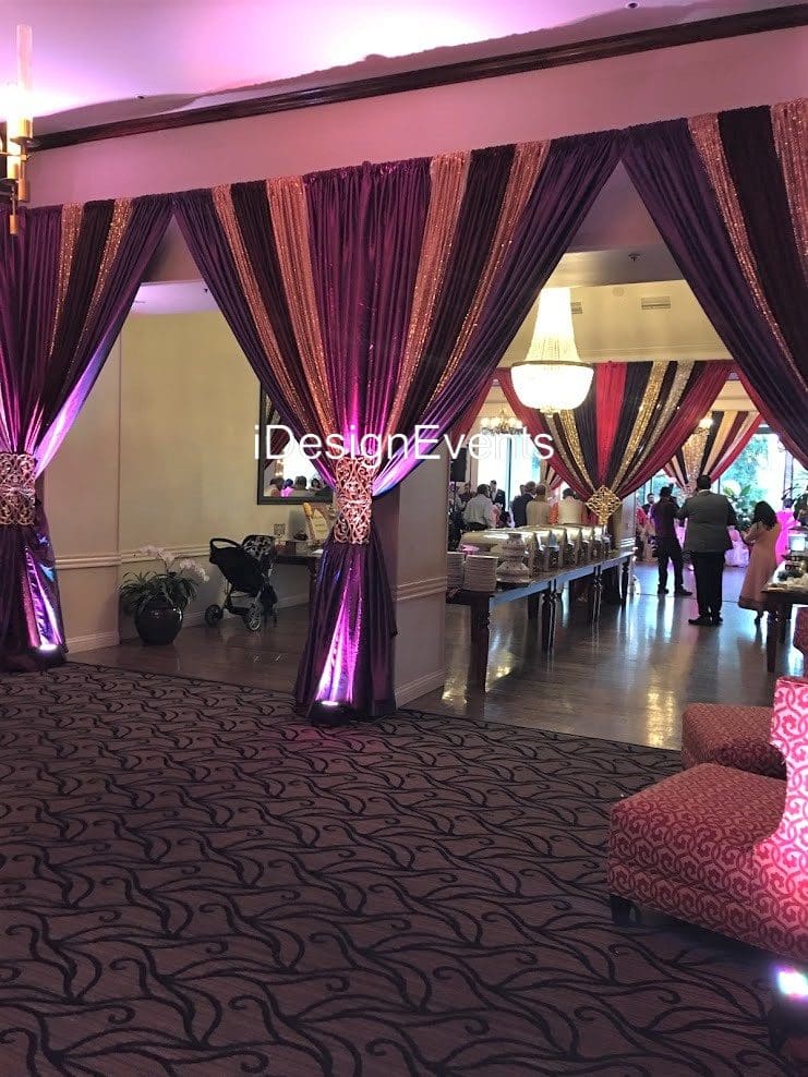 Elegant event space with purple drapes and decorated tables for a celebration.