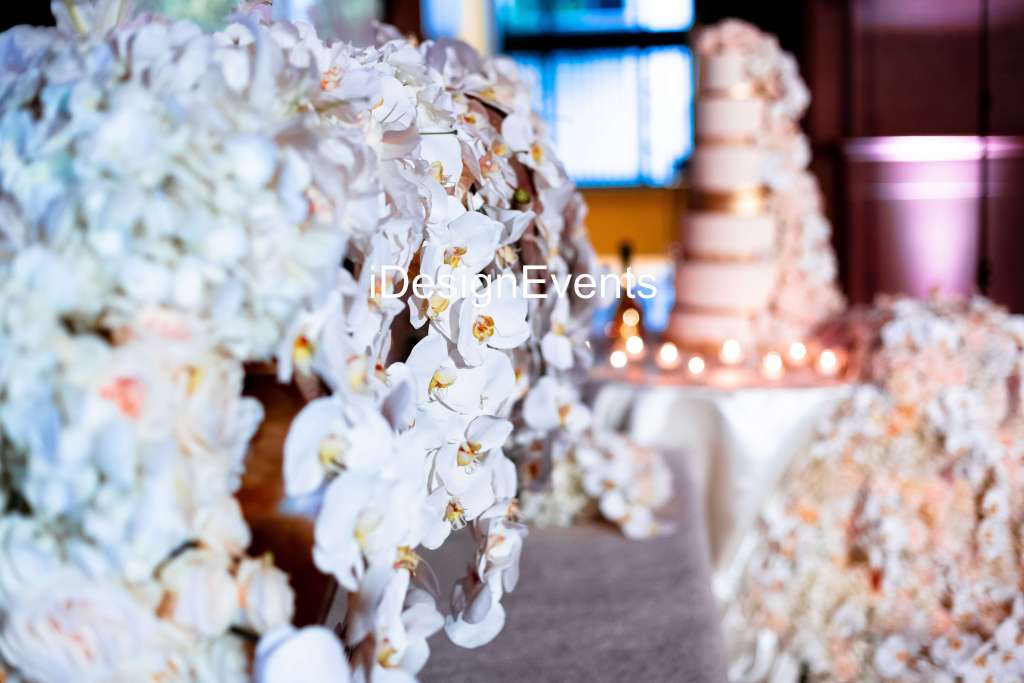 Delicate white floral decorations with a blurred multi-tiered cake in the background.