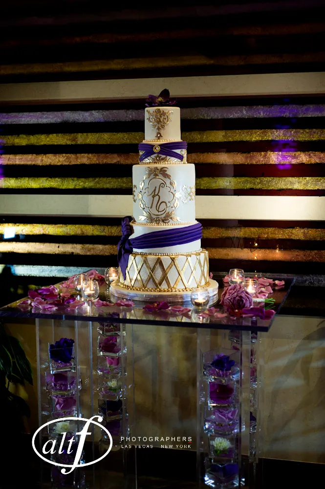 Elegant three-tier wedding cake with purple floral decor and gold accents.
