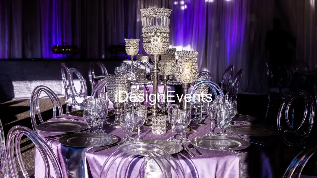 Elegant table setting with crystal glassware and silver accents under purple lighting.