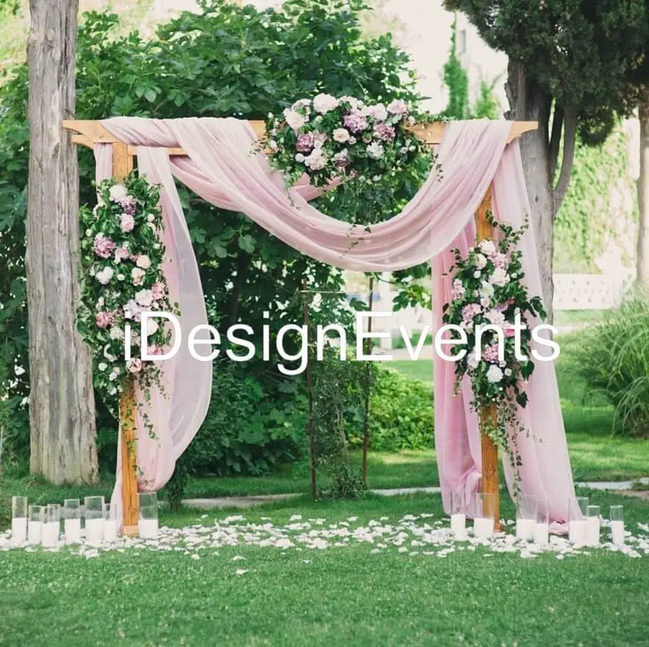 Elegant outdoor wedding arch draped with soft pink fabric and adorned with floral arrangements.