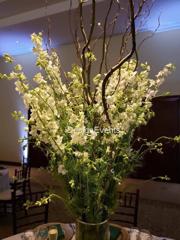 Tall arrangement of delicate white flowers with twisted branches in a vase.
