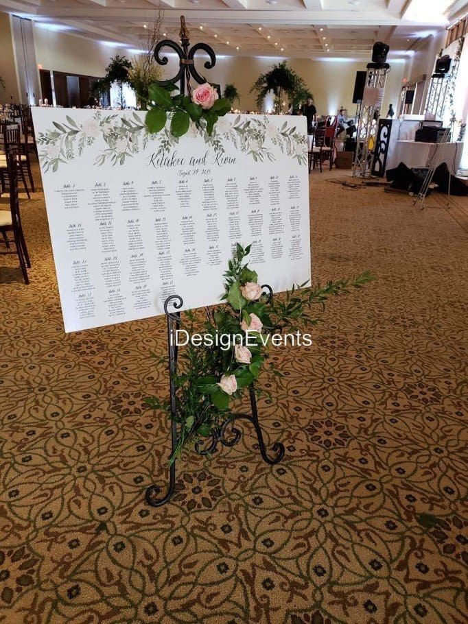 Elegant wedding seating chart with floral decorations on a metal stand.