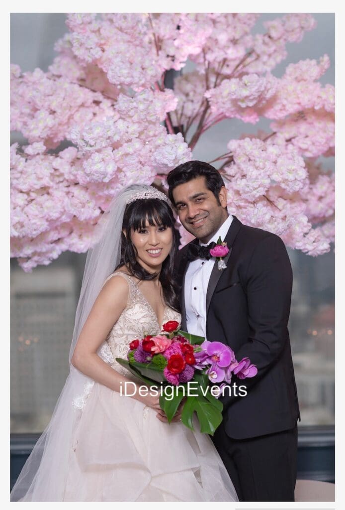 Bride and groom smiling under cherry blossoms on their wedding day.