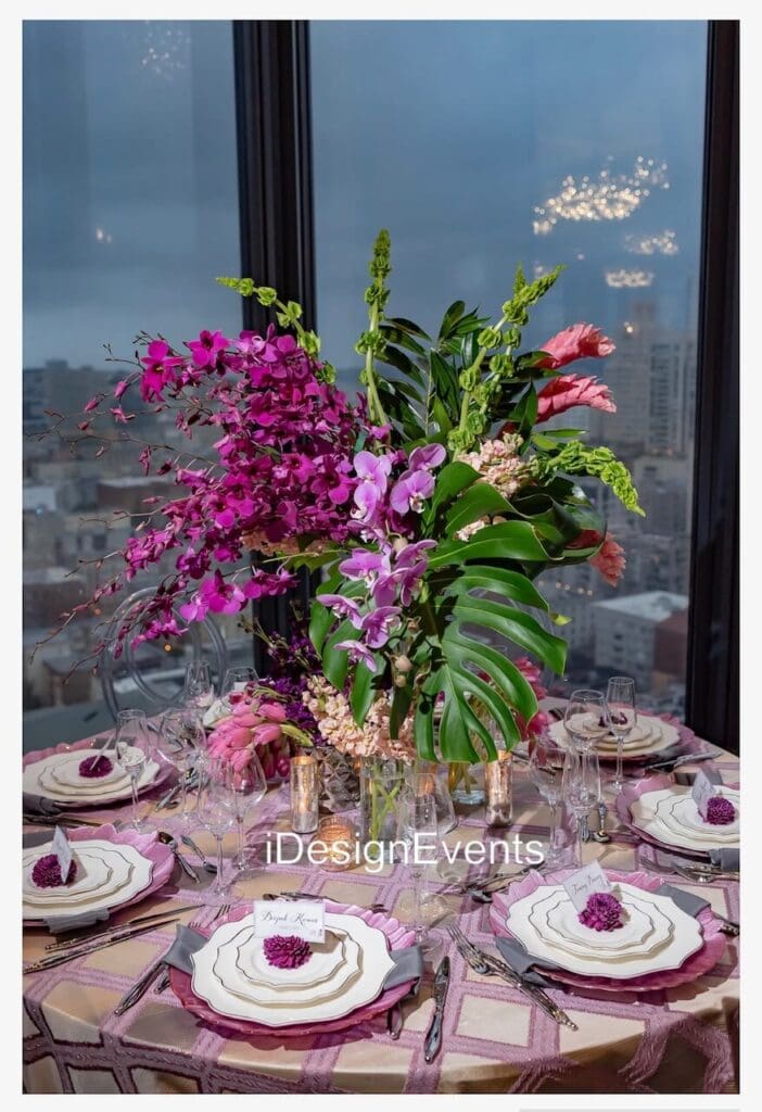 Elegant floral centerpiece with pink orchids and lush greenery on a decorated table.