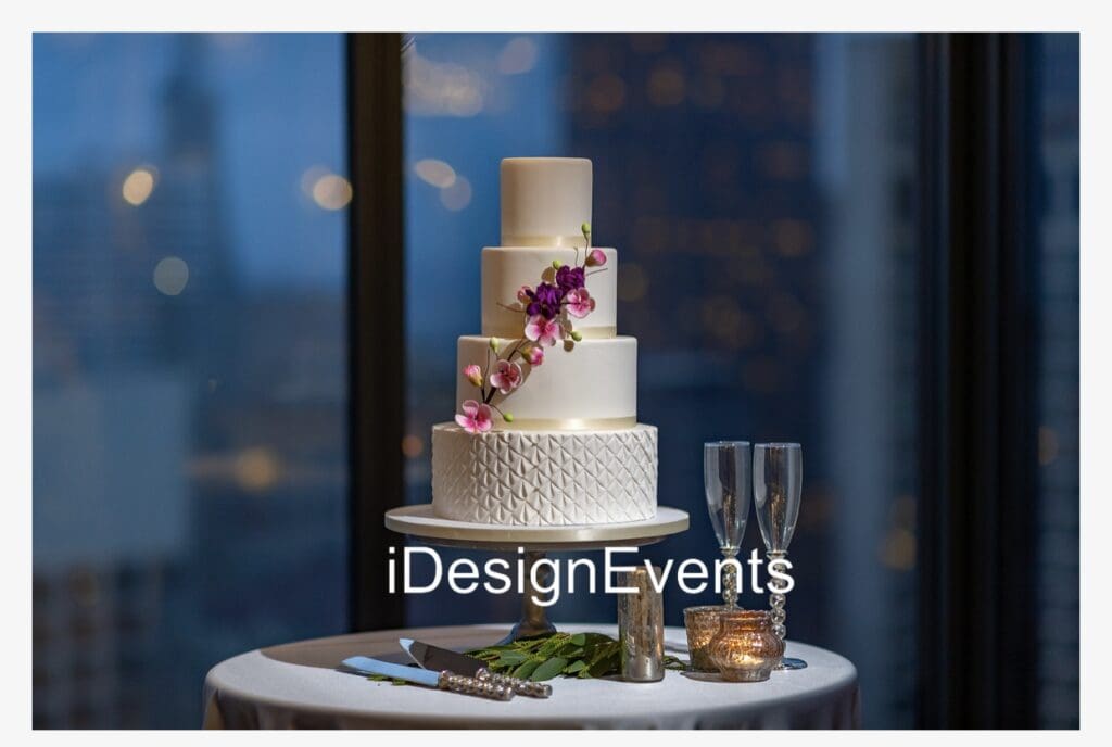 Elegant three-tier white wedding cake adorned with purple flowers and gold accents.