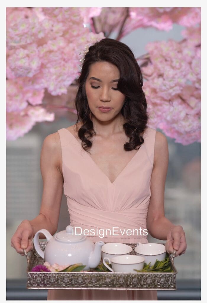 Woman in a pink dress standing behind a table with a cake and floral backdrop.