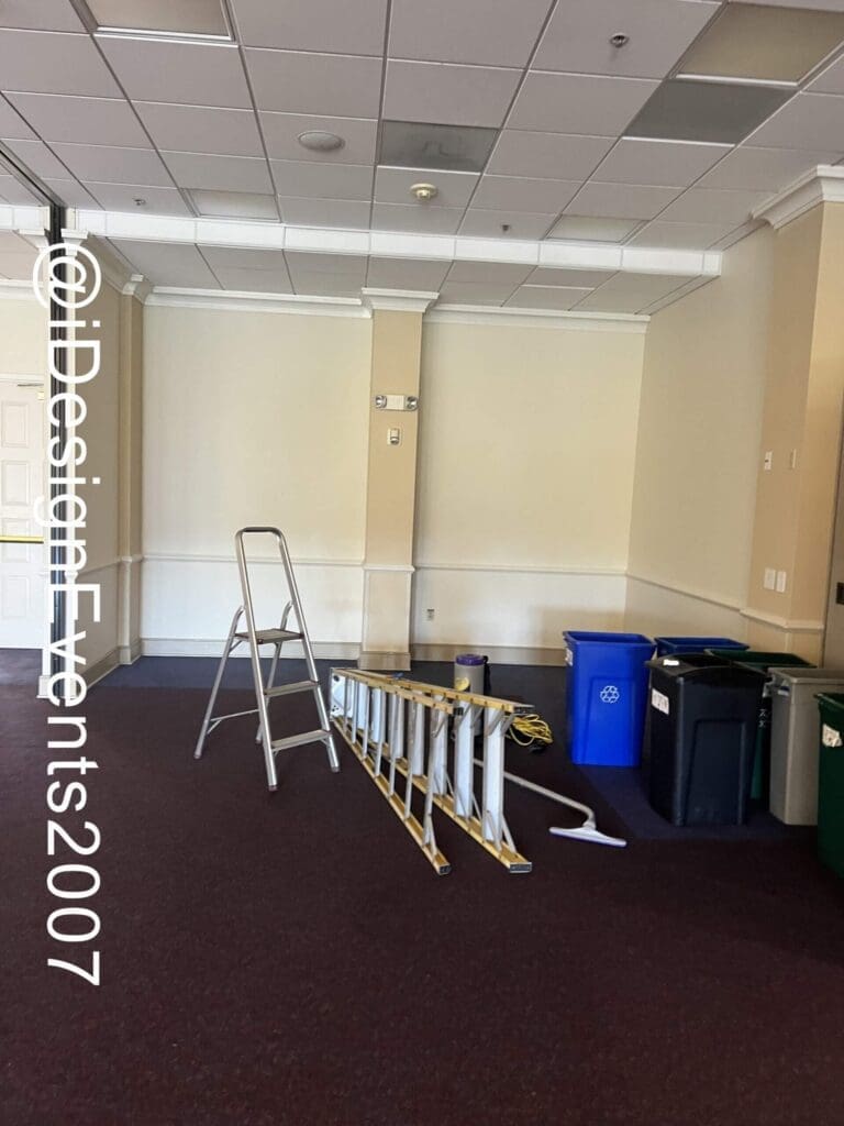 Room with a ladder, long wooden plank, and several trash bins against the wall.