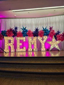 Illuminated REMY sign with colorful feather decorations on stage.
