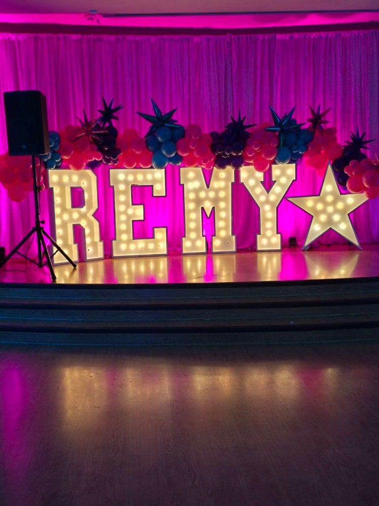 Illuminated marquee letters spelling REMY with a star on a stage.