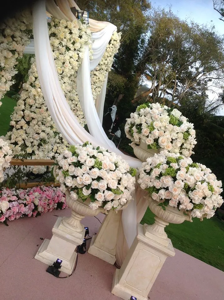 Elegant floral arrangement with white roses and draped fabric at an outdoor event.